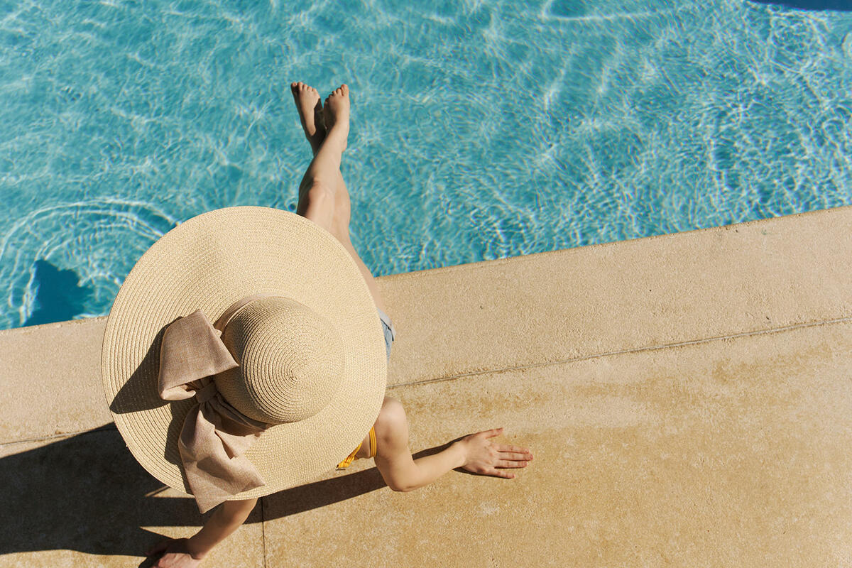 Frau mit Sonnenhut relaxt am Pool