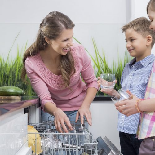 Happy mother and children placing glasses in dishwasher